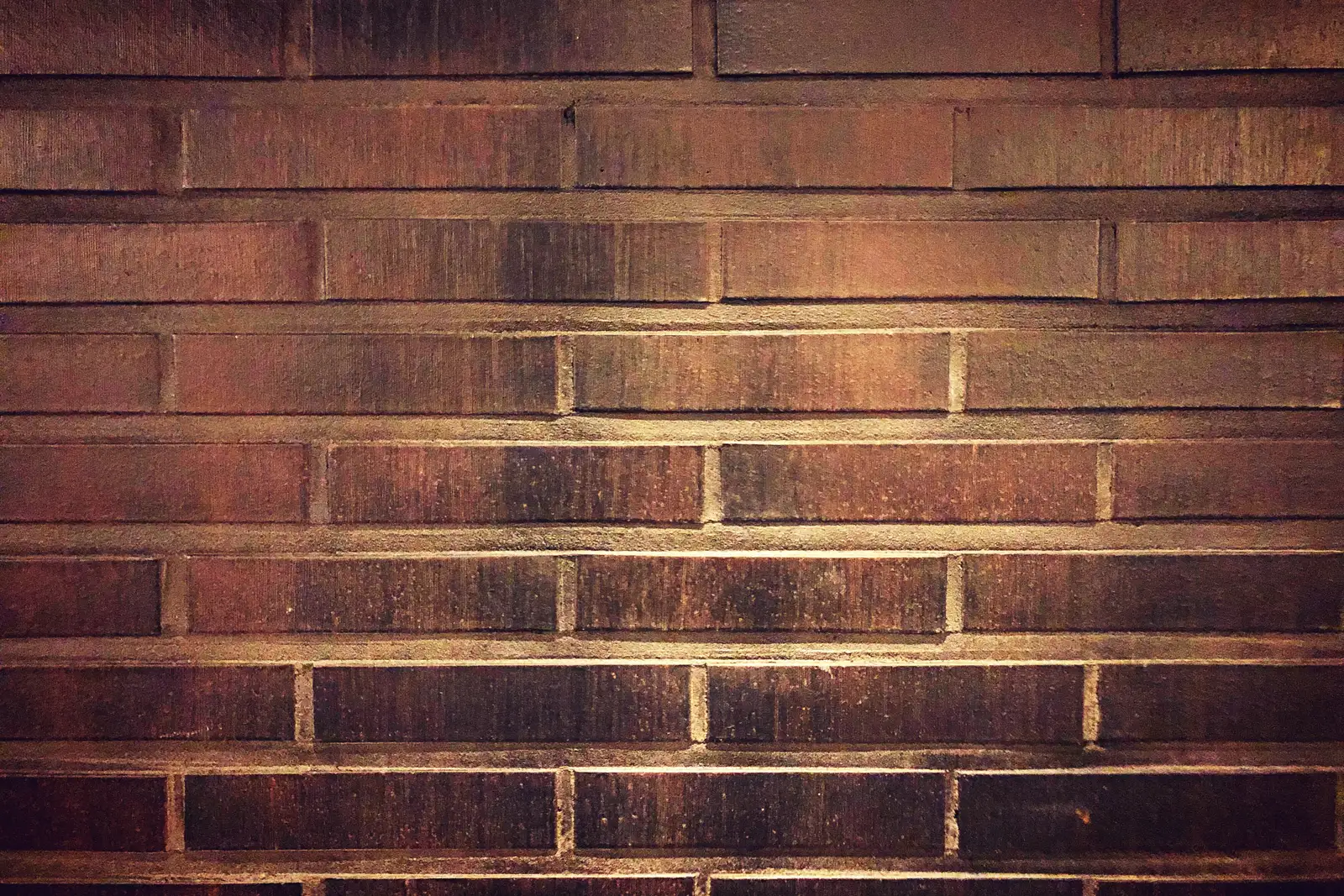 Eine Mauer aus dunkelroten Ziegeln, Reihe für Reihe versetzt gemauert, mit hellen Fugen und einem warmen Lichtstreifen quer über der Mitte.